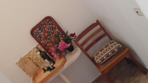 Een kleine kamer met een houten stoel, een tafel met een dienblad met bloemendesign, en een klein krukje.