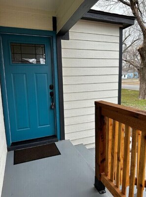 Welcome to a charming home with a distinctive blue door, set within a white exterior and surrounded by a tree and a neighboring house.