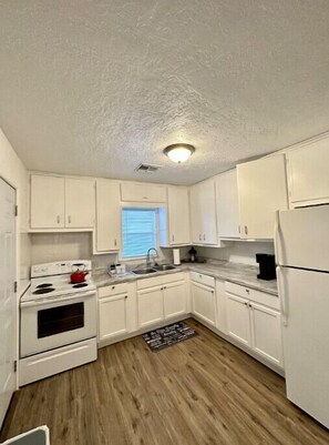 A kitchen with white cabinets, a stove, a sink, and a window.