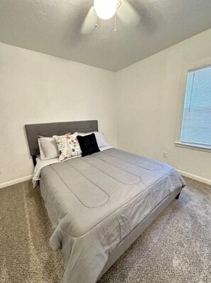 A bedroom with a grey bed, a grey headboard, and a ceiling fan.