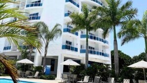 Ein hohes, modernes Hotel mit geschwungener Fassade, einem Schwimmbad und Palmen.