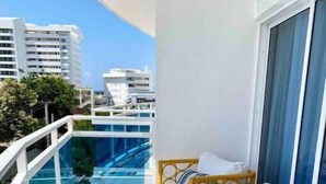 Ein Balkon mit Glastrennwand, zwei Korbstühle mit Kissen und Blick auf die Stadtlandschaft.