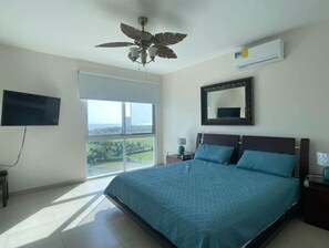 Ein Schlafzimmer mit Bett, Deckenventilator, Fernseher, Fenster und Klimaanlage.