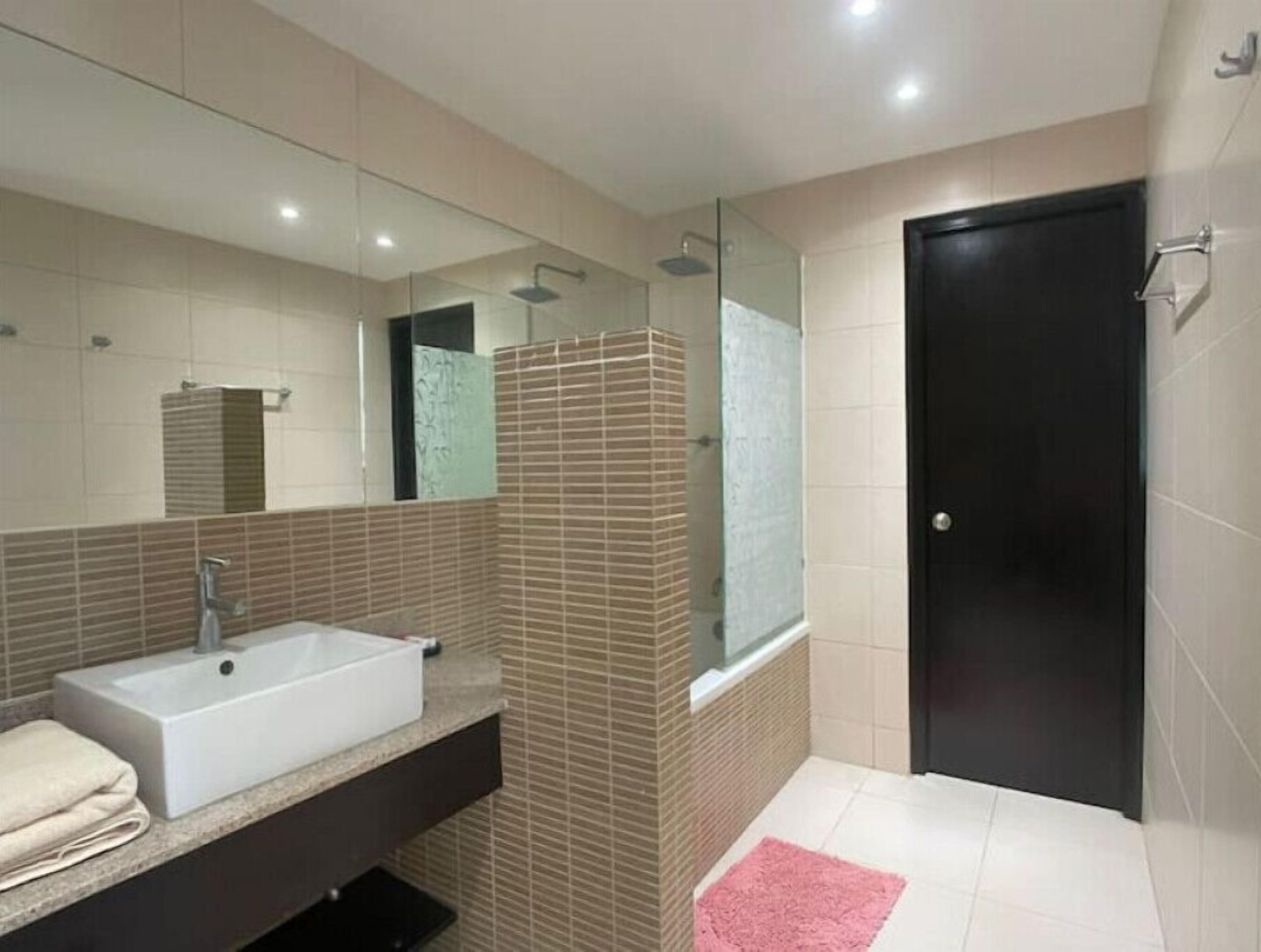 A modern bathroom with a large sink, a glass shower enclosure, and a black door.