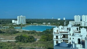 Vista costera con una piscina grande, edificios blancos y un cielo azul despejado.