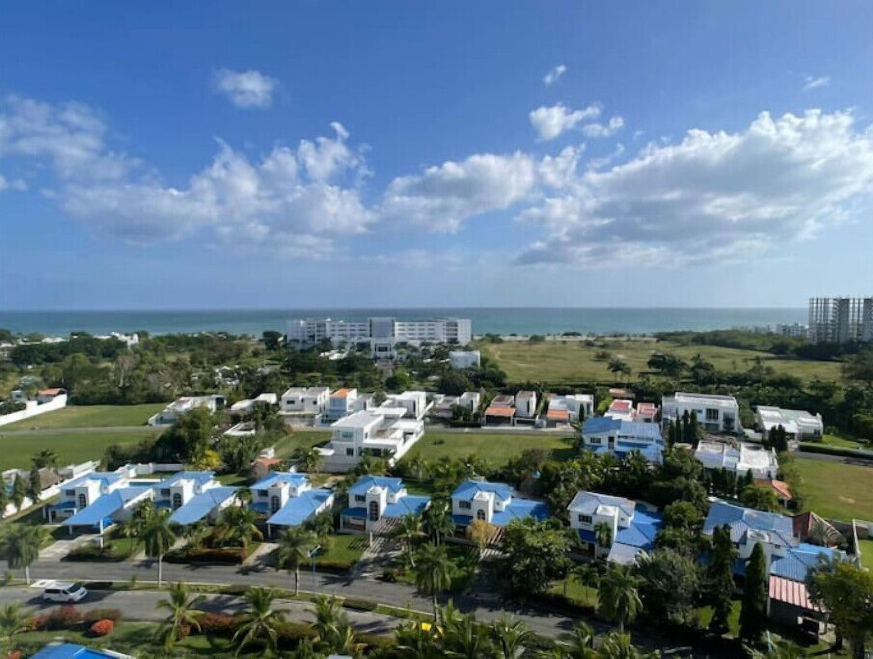 Uma área de resort costeira com vários edifícios, alguns com telhados azuis, e vista para o oceano.