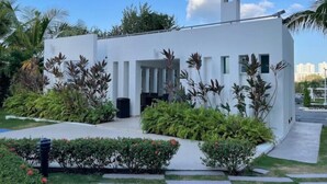 Un edificio moderno blanco con techo plano, rodeado de exuberante vegetación y palmeras.