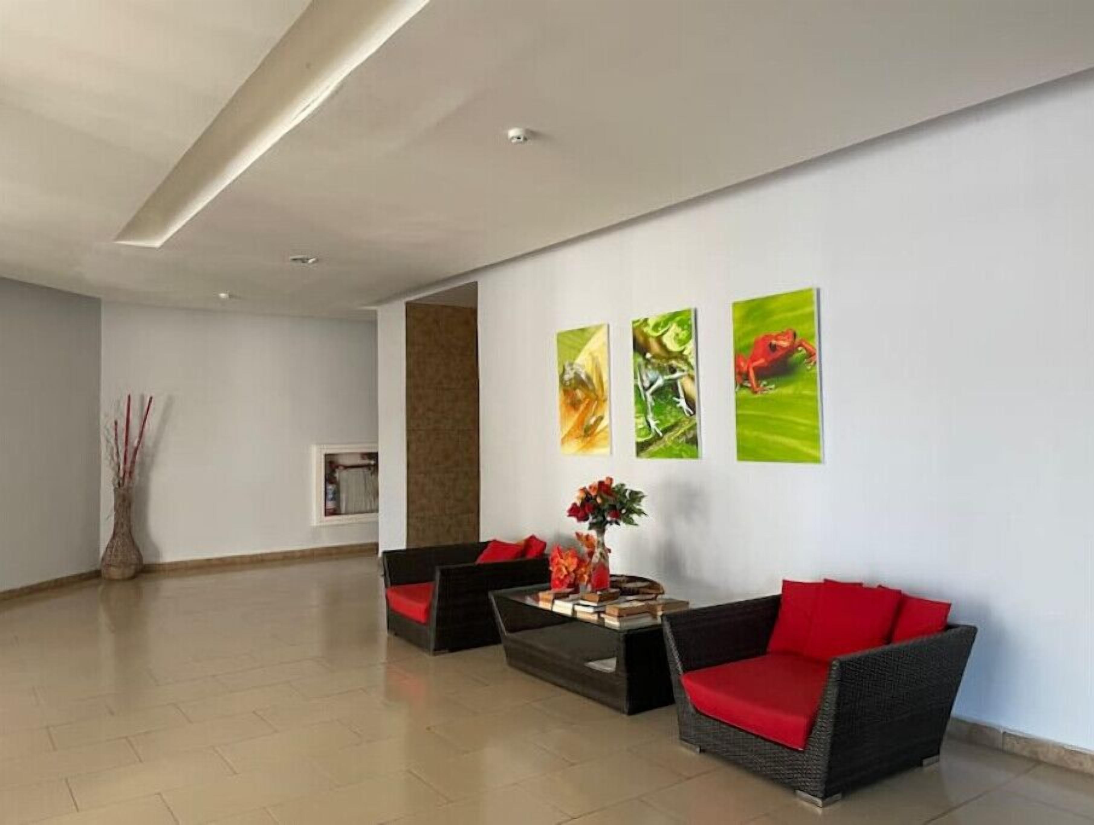 Una habitación amplia con un diseño moderno, que cuenta con un sofá negro y rojo, una mesa de centro de vidrio y tres cuadros en la pared.