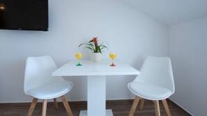 A modern room with a white table, two white chairs, a potted plant, and two glasses of orange juice. - Apartments Horizon - Double Room With Balcony and Sea View (Dubrovnik)