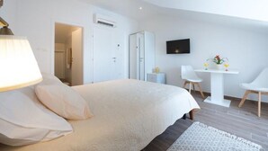 A modern hotel room with a large bed, a desk, a chair, and a TV mounted on the wall. - Apartments Horizon - Double Room With Balcony and Sea View (Dubrovnik)