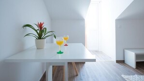 A modern, minimalist room with a white table, a potted plant, and two glasses of orange juice. - Apartments Horizon - Double Room With Balcony and Sea View (Dubrovnik)