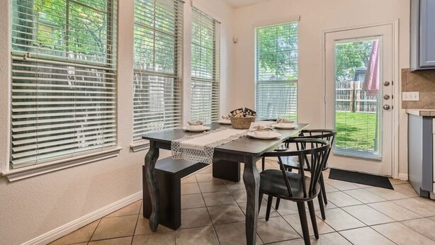 A dining area with a table set for four, surrounded by large windows with blinds, a ceiling light fixture, and a view of a backyard. - Spacious 6-bedroom Duplex  w/Pool Mins FC Stadium / Domain (Austin)