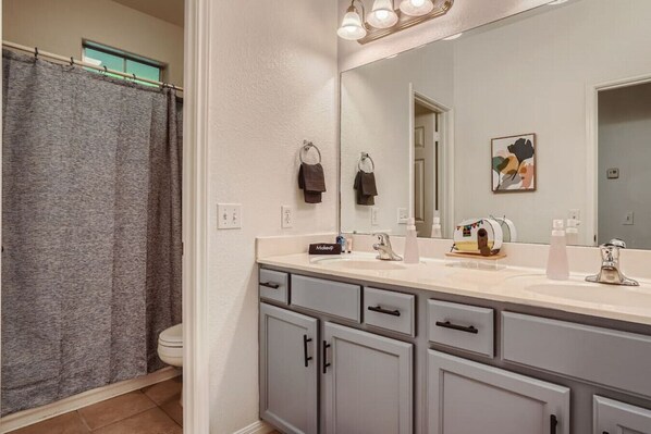 Une salle de bain avec un rideau de douche, un lavabo avec un miroir et des toilettes.