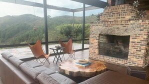 A modern outdoor seating area with a brick fireplace, leather sofa, and two chairs. - Casa Pionono (Guasca)