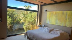 A bedroom with a large window, a bed, and a yellow abstract painting on the wall. - Casa Pionono (Guasca)