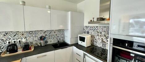 A modern kitchen with white cabinets, a black countertop, a microwave, a toaster, and a built-in oven.
