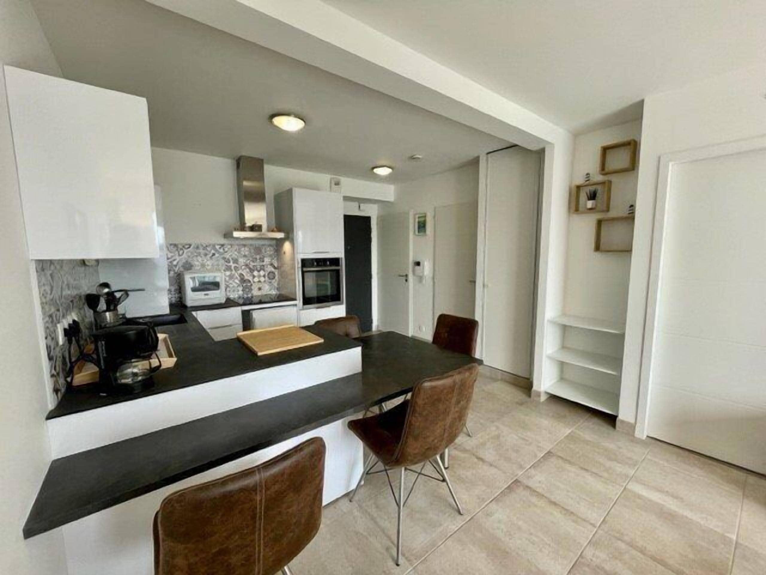 A modern kitchen with a black countertop, white cabinets, a built-in oven, and a dining area with two chairs.