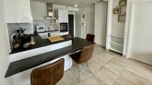 A modern kitchen with a black countertop, white cabinets, a built-in oven, and a dining area with two chairs. - Quiberon - 2 rooms apartment - 40m² - quiet area (QUIBERON)