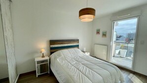 A bedroom with a bed, bedside table, lamp, and a view through a window. - Quiberon - 2 rooms apartment - 40m² - quiet area (QUIBERON)