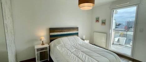 A bedroom with a bed, bedside table, lamp, and a view through a window.