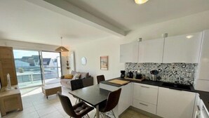 A modern kitchen with white cabinets, a black countertop, and a dining area with a table and chairs. - Quiberon - 2 rooms apartment - 40m² - quiet area (QUIBERON)
