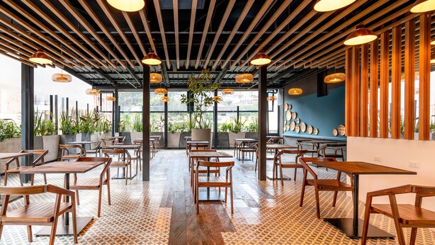 A restaurant interior with wooden tables and chairs, a patterned floor, and hanging pendant lights. - Hotel Faranda Collection Zona G (Bogotá)