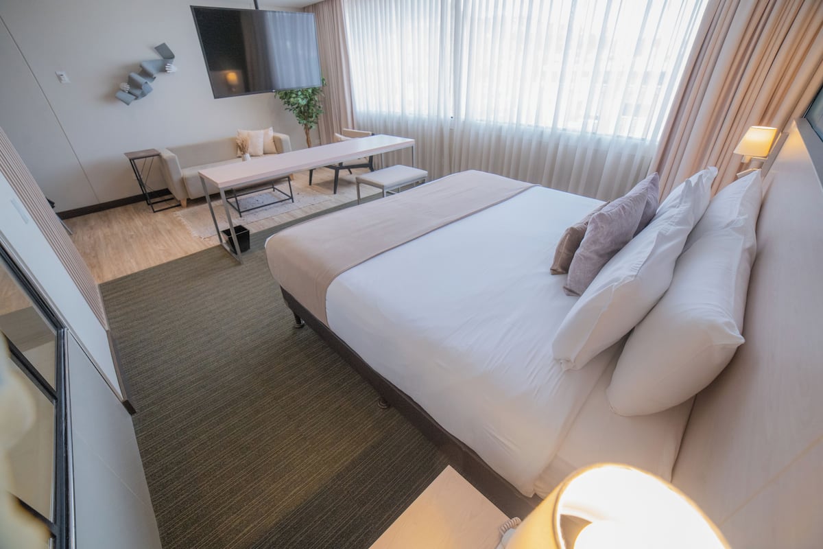 A hotel room with a large bed, a desk, a chair, and a television on the wall.