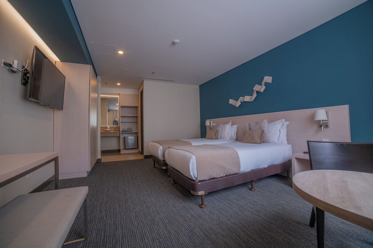 A hotel room with a large bed, a desk, a chair, and a TV.