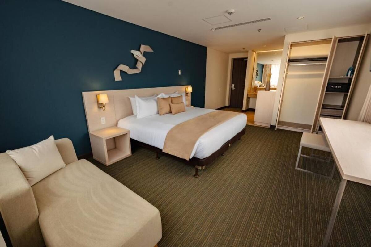 A hotel room with a bed, bedside tables, a desk, and a wardrobe.