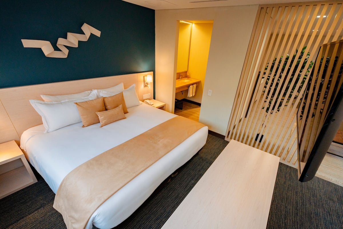 A modern hotel room with a large bed, bedside table, and a nightstand.