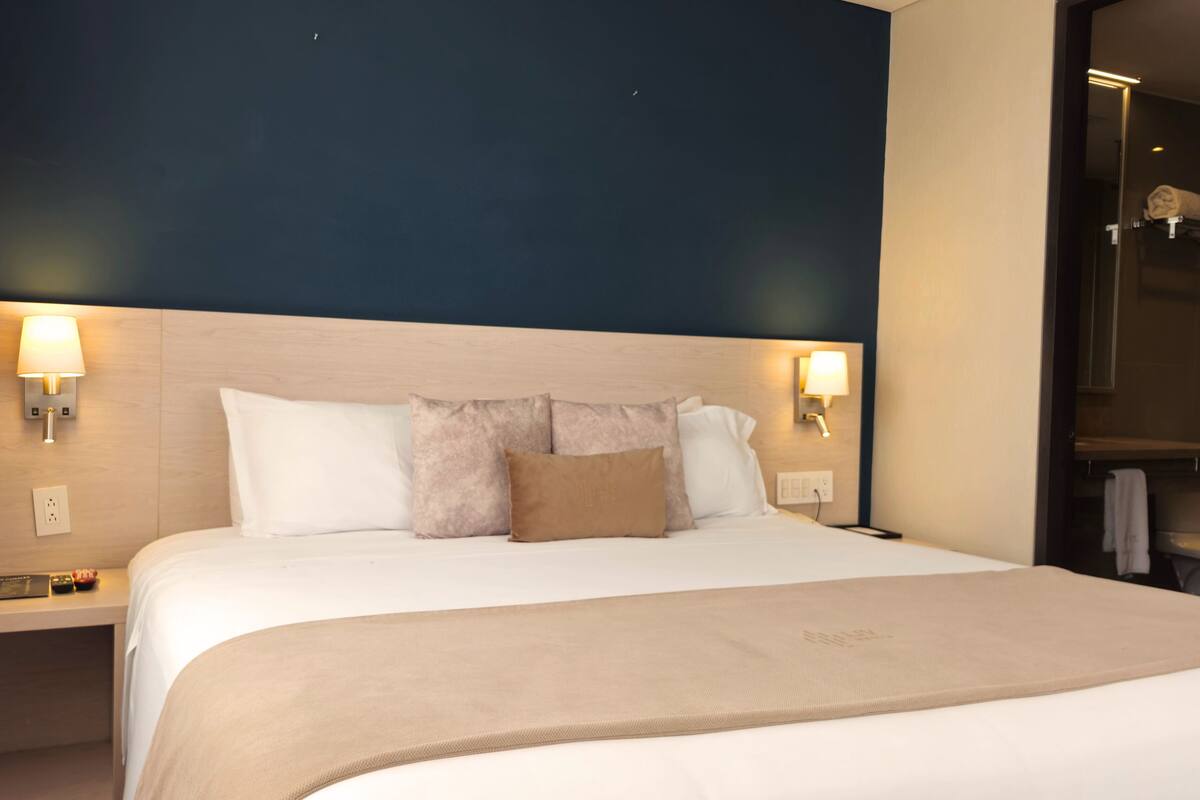 A hotel room with a large bed, two bedside lamps, a wooden headboard, and a dark blue accent wall.