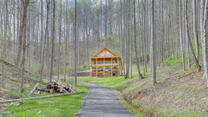 Une cabane dotée d’un balcon, entourée d’une zone boisée et accessible par un chemin pavé.
