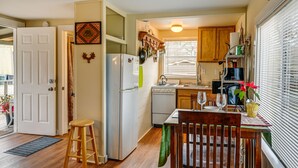 Une cuisine compacte équipée d’un réfrigérateur, d’une cuisinière et de meubles de rangement en bois. Une table à manger avec des chaises est placée près de la fenêtre.