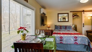 Une chambre avec un lit, une table dressée pour deux personnes, une fenêtre avec des stores et un climatiseur fixé au mur.