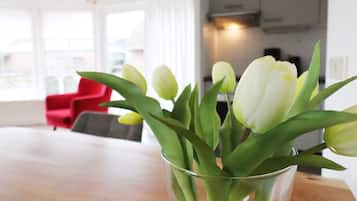 Un soggiorno con un vaso di tulipani bianchi su un tavolo di legno, una sedia rossa e una cucina sullo sfondo.