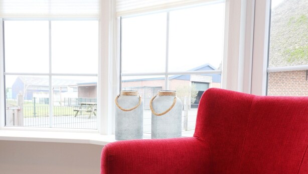 A red armchair by a window with a view of buildings and a fence.