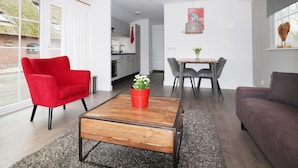 A modern living room with a red chair, a wooden coffee table with a potted plant, a dining table with chairs, and a grey sofa.