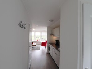 Een moderne keuken met witte kasten, een rode stoel en een raam met uitzicht op het landschap.