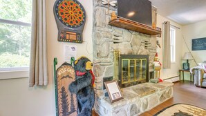 A room with a stone fireplace, a dartboard, a stuffed bear, and a television mounted above the fireplace. - Private Hot Tub & Covered Deck: Cozy Whittier Gem (Whittier)