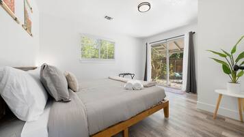 A bedroom with a bed, a window with blinds, a potted plant, and a view of the outdoors.