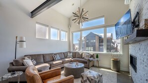 Ein geräumiges Wohnzimmer mit einer großen Eckcouch, einem runden Couchtisch und einem an der Wand befestigten Fernseher.
