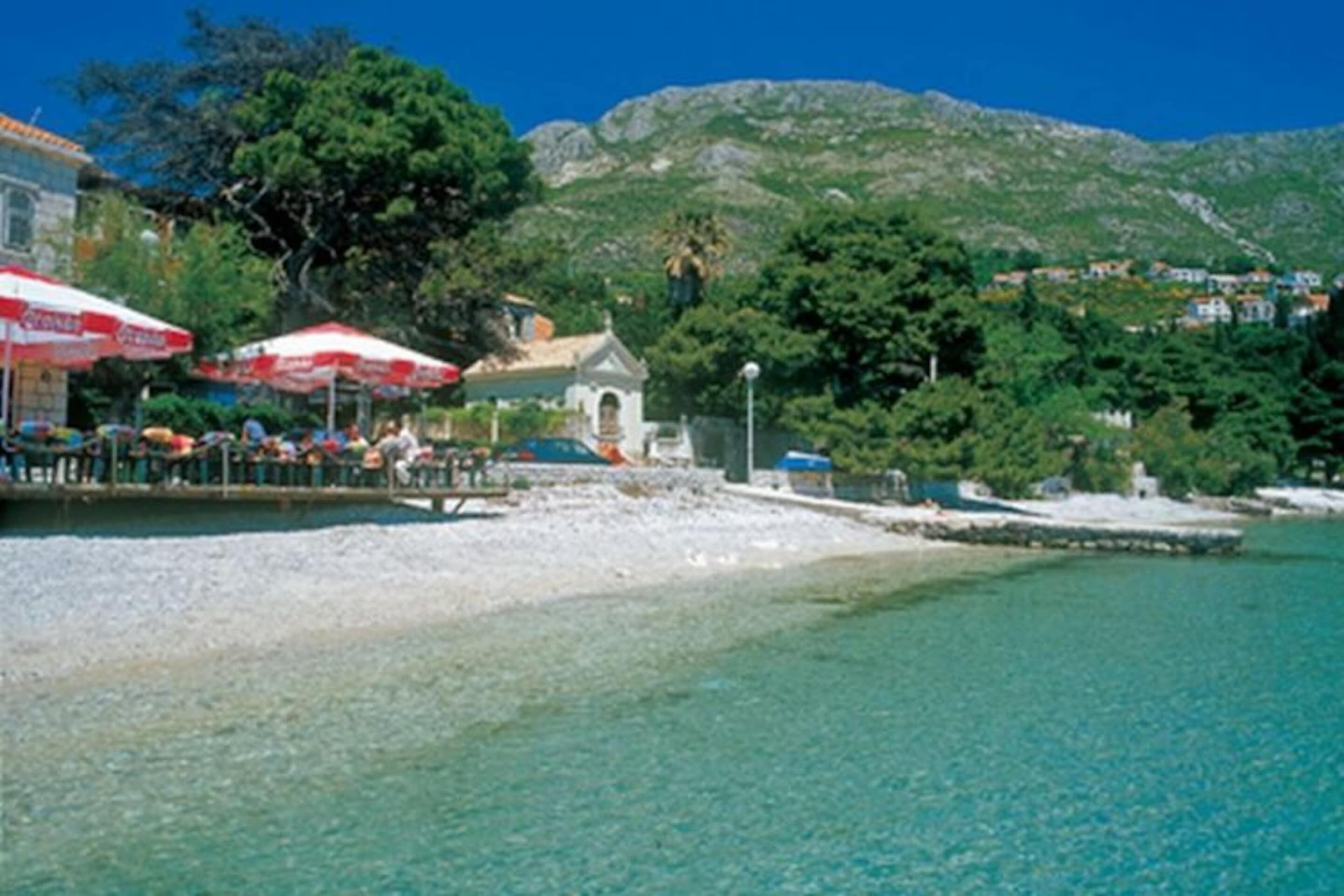 A coastal area with clear turquoise water, a small building, and a rocky hillside in the background.