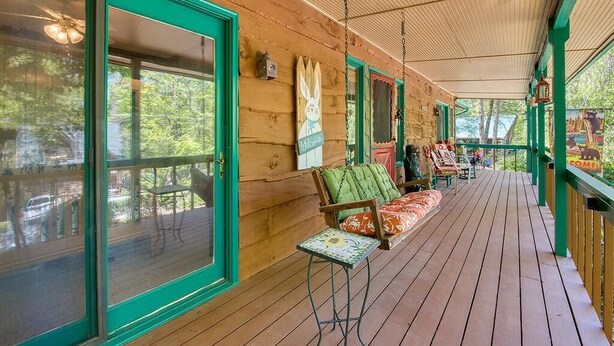 A covered porch with wooden flooring, green-framed windows, and a bench with a cushion. - Fast Wifi, covered porch, and fenced-in yard. Quiet neighborhood. Pet friendly! (Maggie Valley)