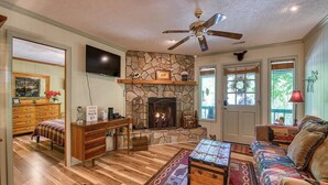 A cozy living room with a stone fireplace, wooden furniture, and a ceiling fan. - Fast Wifi, covered porch, and fenced-in yard. Quiet neighborhood. Pet friendly! (Maggie Valley)