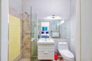 A modern bathroom with a glass shower enclosure, a white sink, a toilet, and a mirror above the sink.