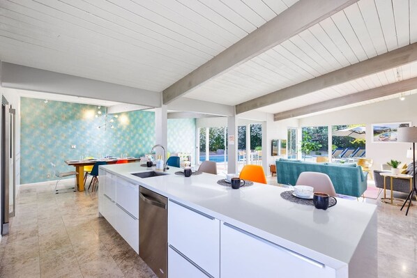 A modern kitchen with a large island, white cabinetry, and a teal backsplash.