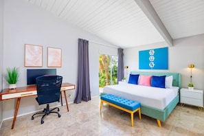 A modern bedroom with a desk, a bed with colorful pillows, a bench, and a large window.