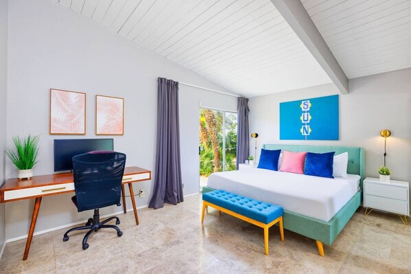 A modern bedroom with a desk, a bed with colorful pillows, a bench, and a large window.
