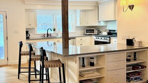 Une cuisine moderne avec des meubles blancs, un îlot central doté de tabourets, un four encastré et un four à micro-ondes.