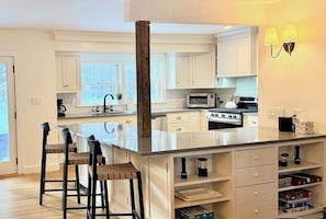 A modern kitchen with white cabinets, a central island with bar stools, a built-in oven, and a microwave.